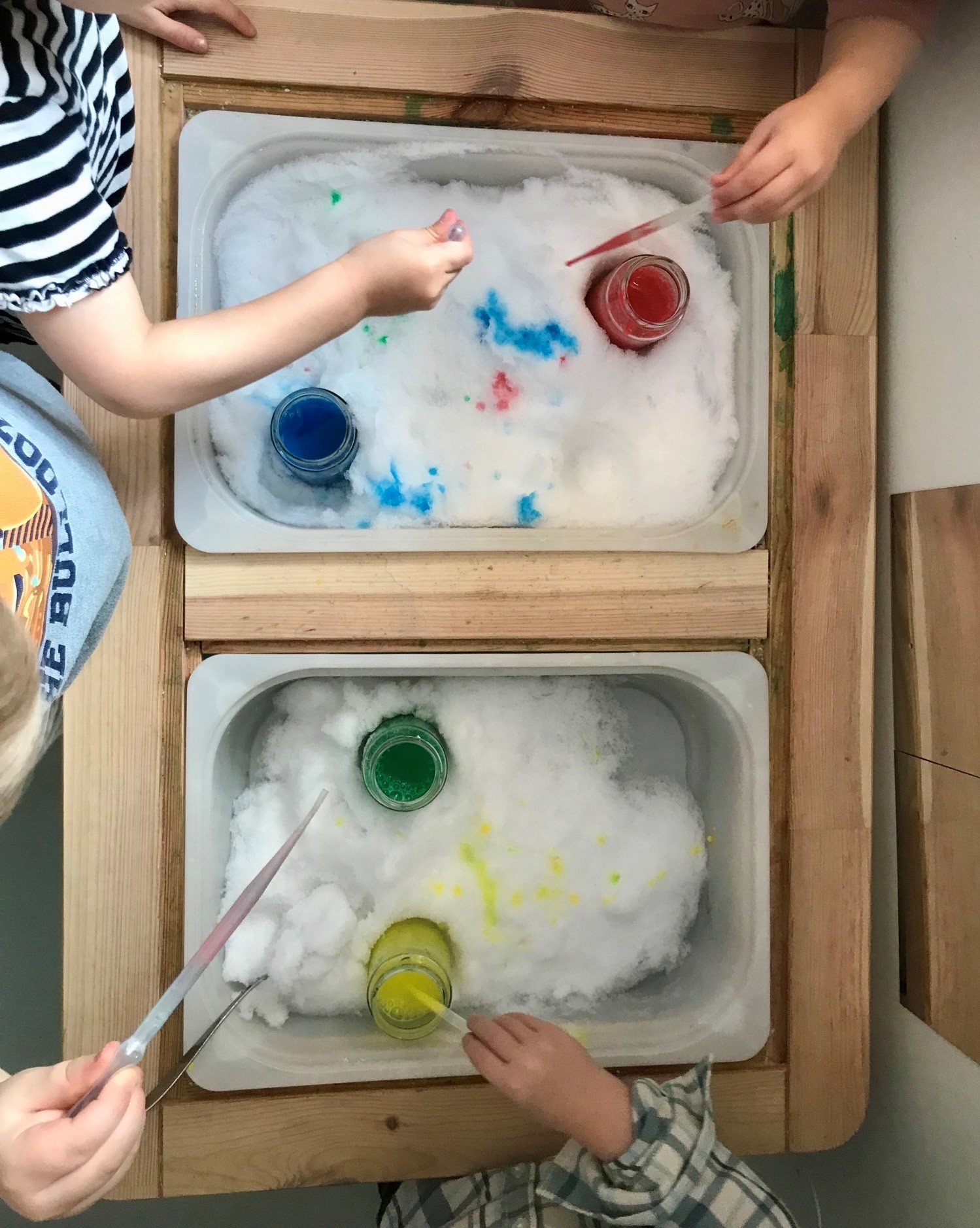 Förskolebarn hos Skrattegi Förskolor målar med vattenfärg på snö i baljor inomhus